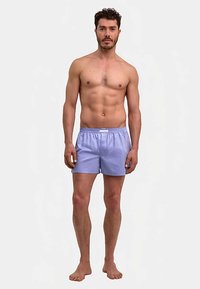 Boxers rayés violet clair avec une ceinture élastique, en tissu lisse. Portés par un mannequin masculin torse nu, debout pieds nus.