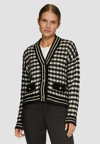 Schwarz-weißer karierter Cardigan mit V-Ausschnitt, goldenen Knöpfen, strukturierten Taschen und gestreiftem Detail entlang des Saums und der Ärmel.