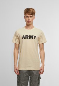 Bēša kokvilnas T-kreklu ar īsām piedurknēm, uz kura krūšu daļas ir izteiksmīgs melns "ARMY" uzraksts. Vienkāršs, ikdienišķs dizains.