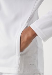 White athletic shirt with a mesh panel at the side, featuring a hidden pocket. "DRYCELL" logo in grey is visible near the hem.