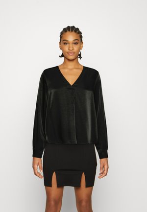 Blusa preta de cetim com decote em V e mangas longas, combinada com uma saia preta ajustada com duas fendas frontais.