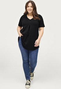 Zwarte V-hals T-shirt met korte mouwen, met een geplooid ontwerp aan de voorkant. Gepaarde met blauwe jeans en zwarte sneakers met witte zolen.