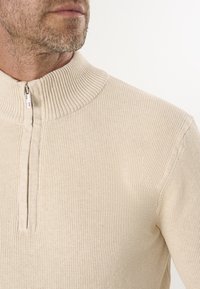 Beżowy sweter z wysokim ściągaczem i pół zamkiem, z teksturowanym wzorem dzianiny i dopasowanym krojem.