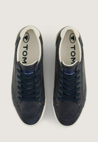 Pantofi sport din piele navy cu talpă din cauciuc albă, având un finisaj texturat, șireturi navy și un logo pe limba pantofului.