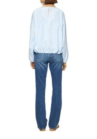 Blusa a righe blu e bianche con vita arricciata e dettaglio a chiave sulla schiena, abbinata a jeans blue dritti e scarpe chiare.