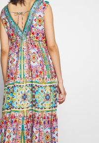 Maxi dress con vivaci motivi floreali e geometrici, dotata di una schiena bassa con lacci, maniche a cappuccio e un design a gonna a strati.