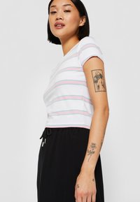Hvit t-skjorte med lyserøde og blå horisontale striper, kortermet, tettsittende design. Svart joggebukser med justerbart liv.