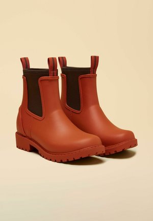 Red waterproof ankle boots with a smooth rubber exterior, elastic side panels in dark brown, and textured soles for grip.