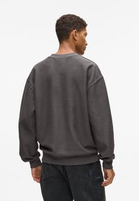 Tmavo šedý oversize mikina s textúrovaným povrchom, rebrovanými manžetami a pásom, s okrúhlym výstrihom a dizajnom s klesajúcim ramenom.