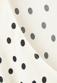 Tissu blanc avec des pois noirs régulièrement espacés, montrant une couture où deux morceaux sont assemblés.