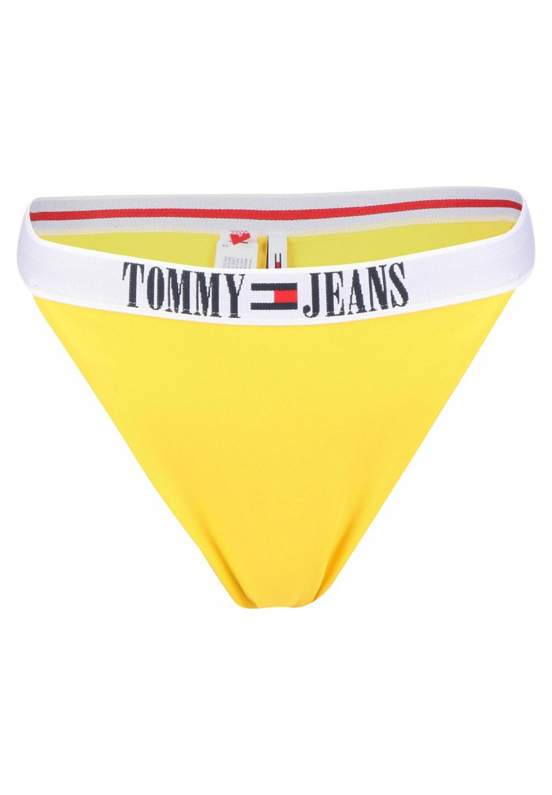 Bañador amarillo tipo bikini con una cinturilla elástica blanca que presenta la marca "TOMMY JEANS" en letras negritas negras; textura de tela suave.
