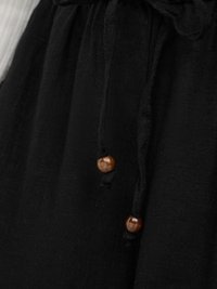 Gros plan sur un tissu noir avec deux perles en bois attachées à des cordons noirs noués en haut.