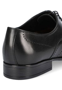 Czarny skórzany but z zaokrąglonym tyłem, dekoracyjnymi perforacjami i niskim, teksturowanym podeszwą gumową. Posiada gładką powierzchnię i sznurowadła.