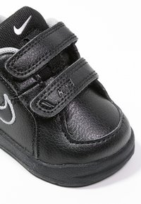 Černé kožené boty Nike pro batolata s suchým zipem, kulatou špičkou, texturovaným povrchem a bílým logem na boku.