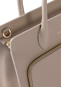 Sac en cuir beige avec une surface texturée, doté de accents en métal doré et d'une poche zippée à l'avant.