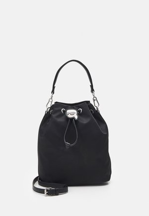 Zwarte bucketbag met trekkoord, enkele bovenste handgreep, afneembare schouderriem en zilveren charm met cartoongezicht aan de voorkant.
