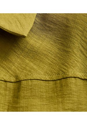 Tela verde oliva con un acabado texturizado. Presenta un cuello doblado y una costura visible a lo largo del dobladillo inferior.