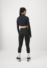Crop top noir à manches longues avec des panneaux texturés, associé à un legging noir taille haute avec un motif côtelé. Chaussettes et chaussures de sport blanches.