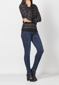 Gebreide trui met meerkleurige horizontale strepen op een donkere achtergrond; gecombineerd met slim-fit blauwe jeans en zwarte hoge enkellaarsjes.