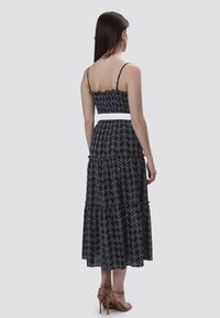Zwart bloemen maxi-jurk met spaghettibandjes en een gerimpelde borstpartij, met een witte tailleband. Gelaagd stof met verfijnde patronen.