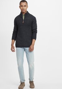 Mörkblå stickad tröja med texturerad mönstrad överdel, halvmudskrage och ribbstickade manschetter, parat med ljusblå jeans och bruna skor.