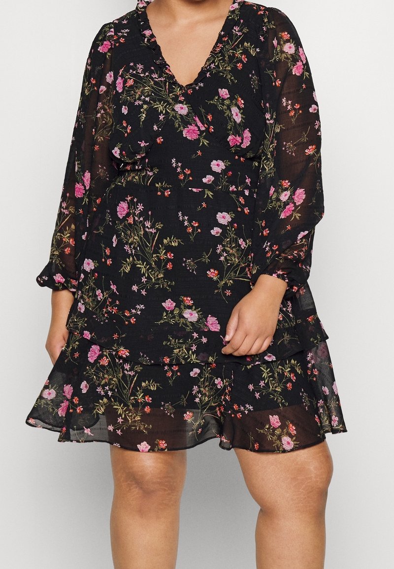Robe noire à fleurs avec de longues manches transparentes, décolleté en V et volants superposés. Présente des motifs floraux roses et verts sur l'ensemble.