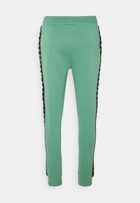 Light green sweatpants with an elastic waistband, tapered legs, and black side stripes featuring a repeating logo pattern.