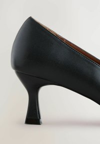 Černá kožená botka na vysokém podpatku s elegantním designem, zúženým podpatkem a texturovaným povrchem s kontrastním hnědým akcentem podél švu.