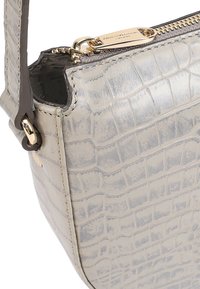 Beige handtas met krokodillenstructuur, gouden ritssluiting en bruine riembevestiging, weergegeven in close-updetail.