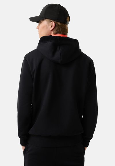 Czarna bluza z kapturem ze sznurkiem, ściągaczami na rękawach i kieszenią kangurką; noszona z czarną czapką. Gładka faktura, klasyczny design.