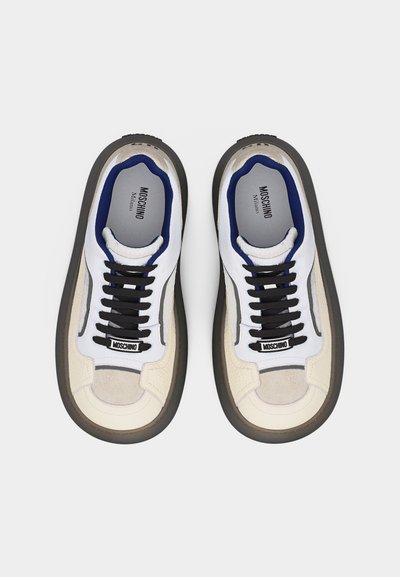 Ζευγάρι λευκά και μπεζ αθλητικά παπούτσια Moschino Milano με μαύρα κορδόνια και μπλε εσωτερική επένδυση, φωτογραφημένα από πάνω σε λευκό φόντο.