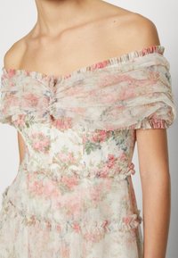 Axelbandslös blommig klänning i genomskinligt tyg med rosa och gröna blommönster, vågiga detaljer och fint hantverk.