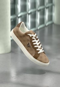 Baskets marron avec un dessus en textile à motifs, des accents en daim rembourrés, des lacets blancs et une semelle en caoutchouc blanche. Présente un triangle de logo sur le côté.