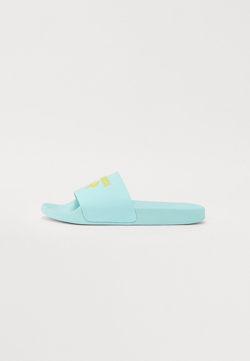 Lyseblå glidesandal med bred stropp og teksturert overflate. Har en gul logo på stroppen. Flat såle.