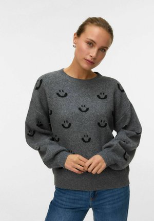 Sweatshirt en tricot gris avec des motifs de visages souriants noirs, col rond, manches amples, et poignets et ourlet côtelés.