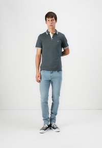 Cămașă polo gri cu guler și manșete în contrast, asortată cu blugi skinny bleu deschis și adidași negri. Design simplu și casual.