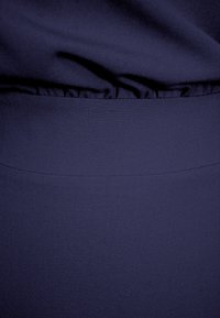 Granatowy materiał o gładkiej fakturze, z marszczoną talią i eleganckim, dopasowanym krojem. Prosty wygląd bez wzorów czy akcentów.