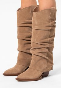 Beige suède laarzen met een slouch-stijl, scherpe neuzen en lage blokhakken. Ze hebben een zachte textuur en een gathered ontwerp dat tot halverwege de kuit reikt.