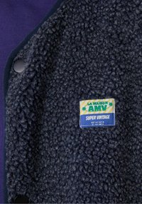 Navy vlnená bunda s fleecovou podšívkou a textúrovaným povrchom. Má okrúhly golier, čierne cvoky a farebnú značku.