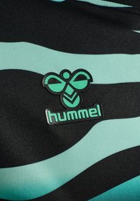 Tejido atlético negro con rayas onduladas turquesas. Presenta un logo de goma negro y turquesa "hummel" y un emblema de abeja en la parte delantera.