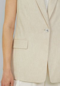 Beige Leinenweste mit einem Reverskragen, einem einzelnen Knopfverschluss und einem dezenten strukturierten Muster; verfügt über eine Seitentasche.