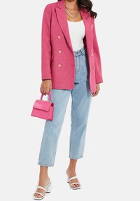 Veste rose croisée, associée à un jean taille haute bleu clair, des sandales blanches à talons et un petit sac à main rose avec une anse tressée.