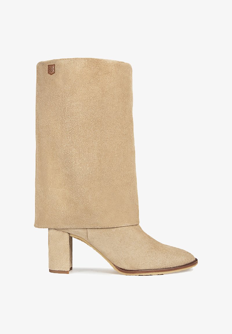 Botín de ante beige hasta el tobillo con un tacón bloques medio y un diseño de solapa. Presenta una punta afilada y un parche de marca cosido en la parte superior.