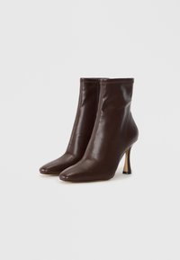 Bottines en cuir marron avec un bout pointu, une silhouette ajustée, un talon aiguille haut et des détails cousus le long du bord supérieur.