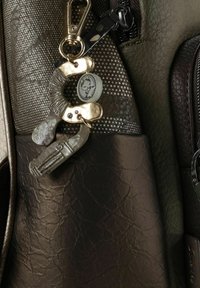 Detail einer braunen Ledertasche mit einem silbernen Schlüsselanhänger im Handschellendesign, einem runden Anhänger und strukturierten Akzenten in dunklen Tönen.