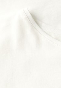Hvid bomulds t-shirt med rund hals og blød tekstur. Har enkel syning langs halsudskæringen og glat, ensartet stof.