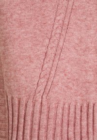 Różowy sweter z dzianiny z teksturowanym wzorem warkocza z jednej strony i prążkowanym wykończeniem na dole, wykonany z miękkiego materiału.