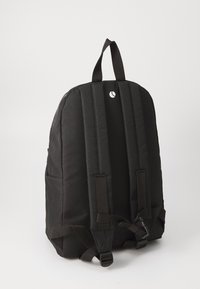 Mochila preta de tecido, com duas alças de ombro acolchoadas, uma pega e um pequeno logo na parte de trás. Design e forma simples.