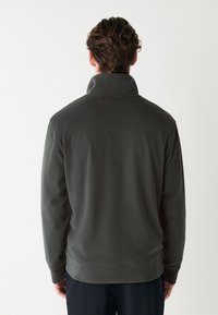 Tumši pelēks vilnas džemperis ar augstu apkakli, garām piedurknēm un ribotu apakšu. Gluda tekstūra, minimālistisks dizains, bez redzamām rakstām vai logotipiem.