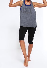 Canotta grigia senza maniche con grafica "IVY PARK" e bordi blu, abbinata a leggings neri fino al ginocchio con accenti bianchi.